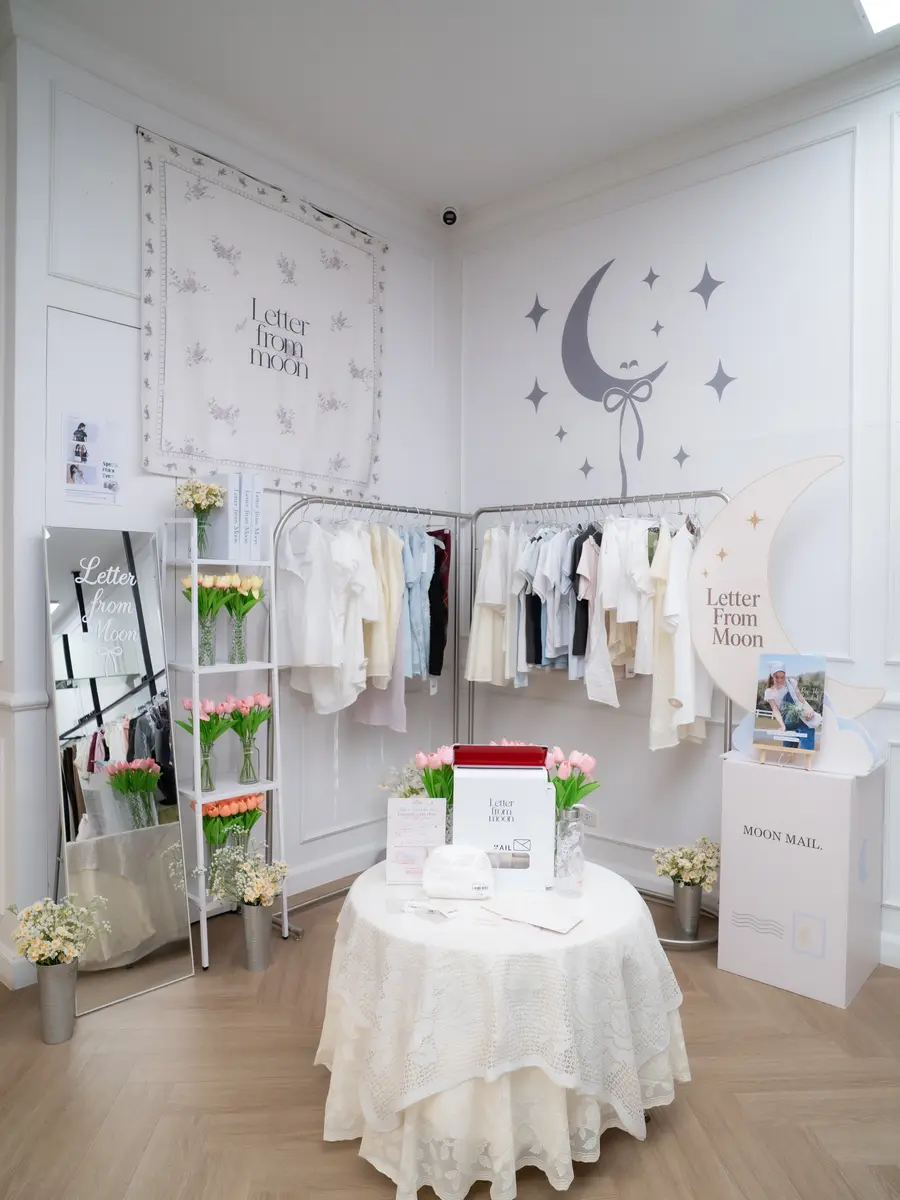 흰 벽에 달과 별 그래픽을 넣은 레터프롬문 브랜드존 — 가운데 원형 테이블과 의류 행어가 놓여 있습니다